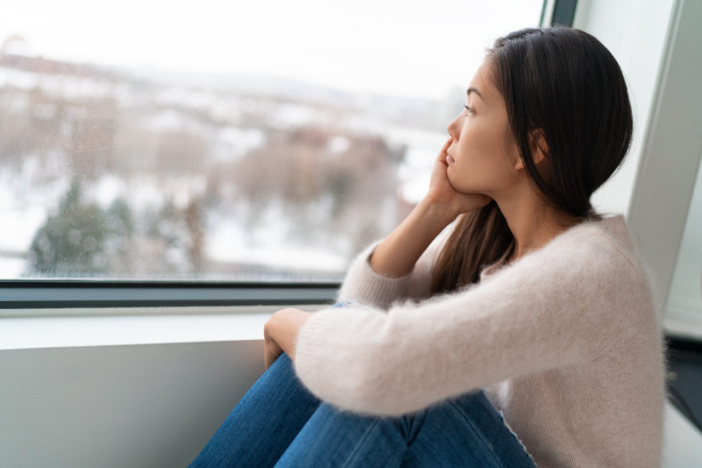 sad girl looking out window during wintertime